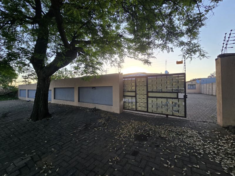 Front exterior view featuring a paved driveway, secure metal gate, and perimeter wall with integrated electric fencing.