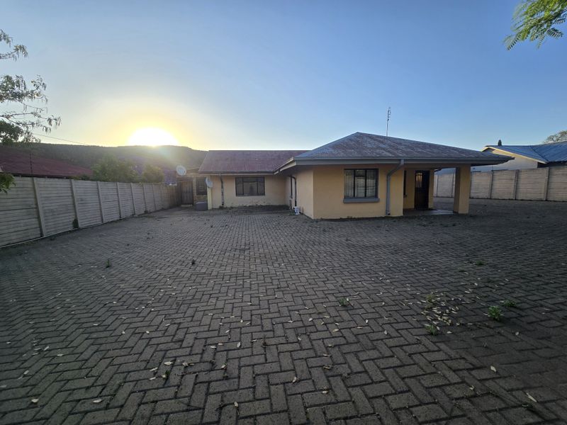 Front view of a single-story house featuring a large paved driveway, covered entrance porch, and perimeter precast concrete walling.