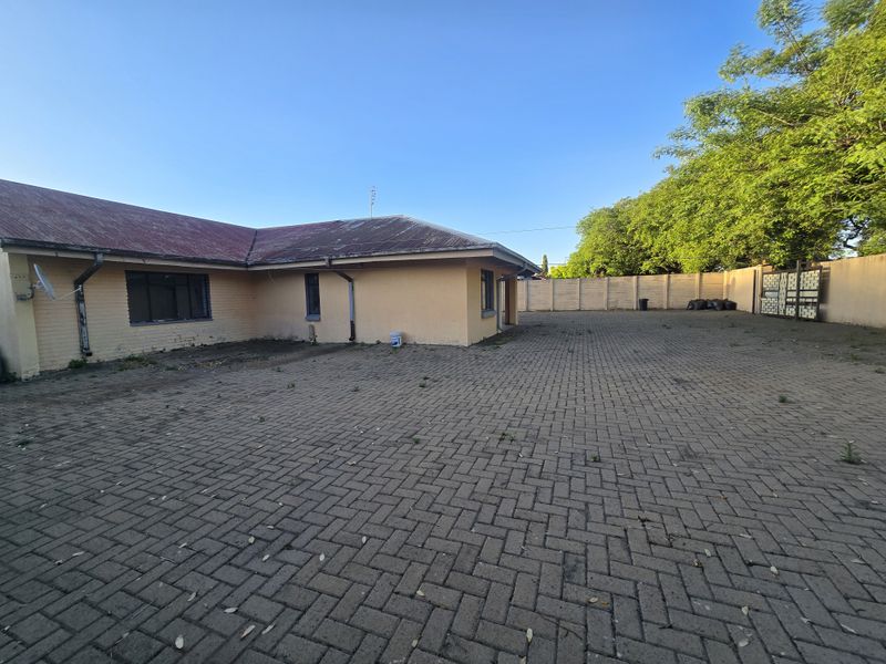 Spacious rear exterior area featuring extensive paved driveway, perimeter precast walling, and a metal gate, with a brick building structure.