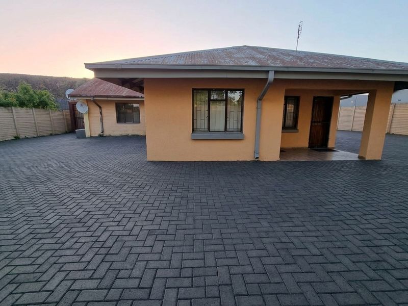 Front view of a single-story house featuring a paved driveway, covered entrance, and secure boundary walls.