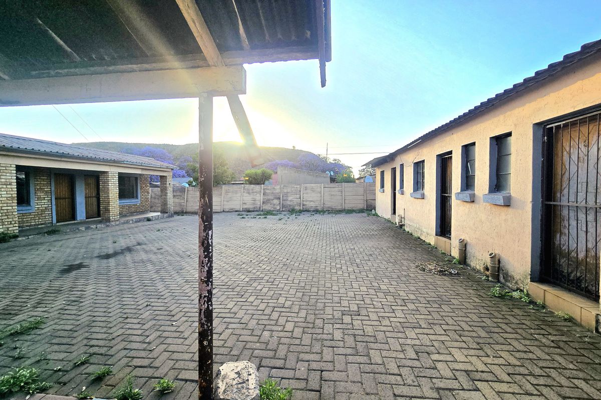 Spacious paved rear courtyard area featuring a covered patio section, secure boundary walling, and multiple access points to the main dwelling.