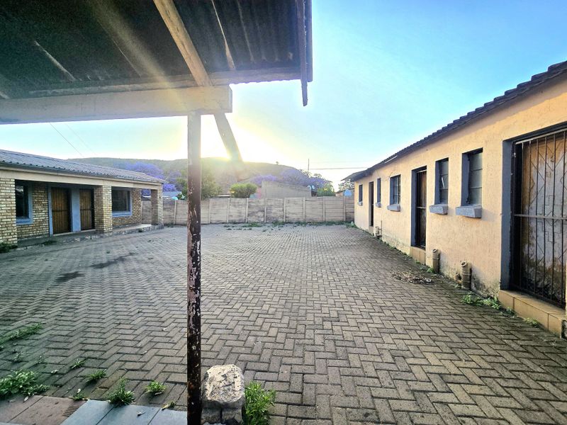 Spacious paved rear courtyard area featuring a covered patio section, secure boundary walling, and multiple access points to the main dwelling.