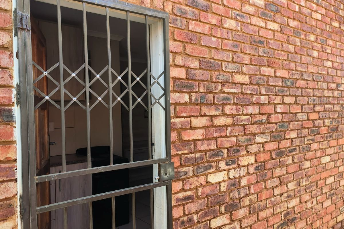 Exterior view of a face brick wall featuring a metal security gate leading into the property.