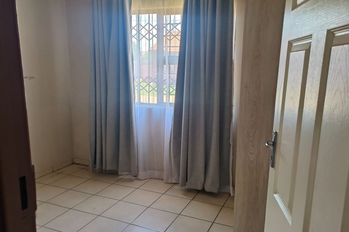 A bright, empty bedroom featuring tiled flooring and a window fitted with a security gate.