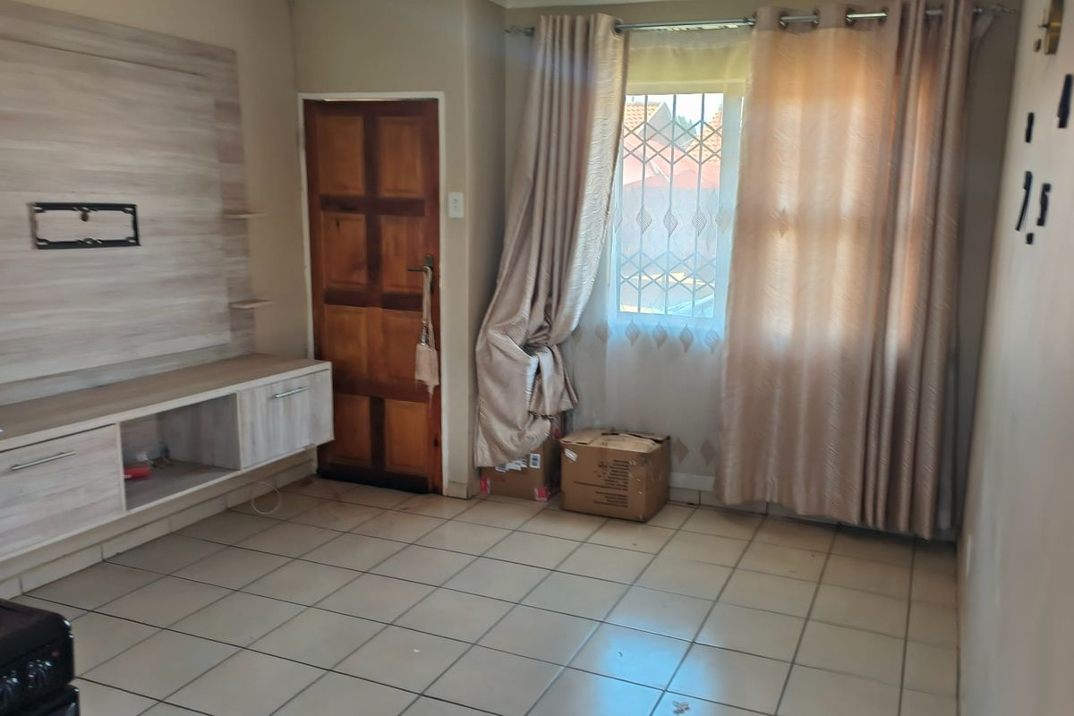 A living room featuring tiled flooring, a built-in media console, and a window with security bars.