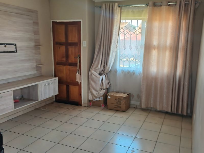 A living room featuring tiled flooring, a built-in media console, and a window with security bars.