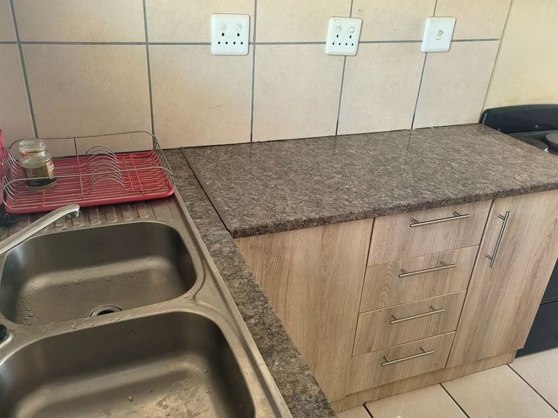 A functional kitchen area featuring a double bowl stainless steel sink, laminate cabinetry, stone-look laminate countertops, and a freestanding stove with tiled splashback.