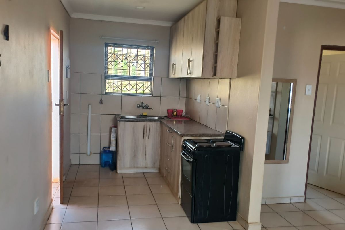 A functional kitchen featuring light wood-finish cabinetry, tiled backsplash, tiled flooring, and a window with security bars, providing a practical cooking and preparation space.