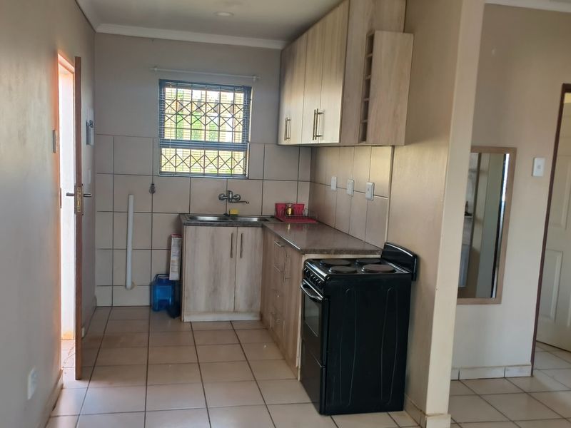 A functional kitchen featuring light wood-finish cabinetry, tiled backsplash, tiled flooring, and a window with security bars, providing a practical cooking and preparation space.