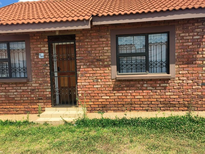 Front elevation of a face brick house featuring terracotta roof tiles, security gates, and aluminium window frames with a paved entrance area.