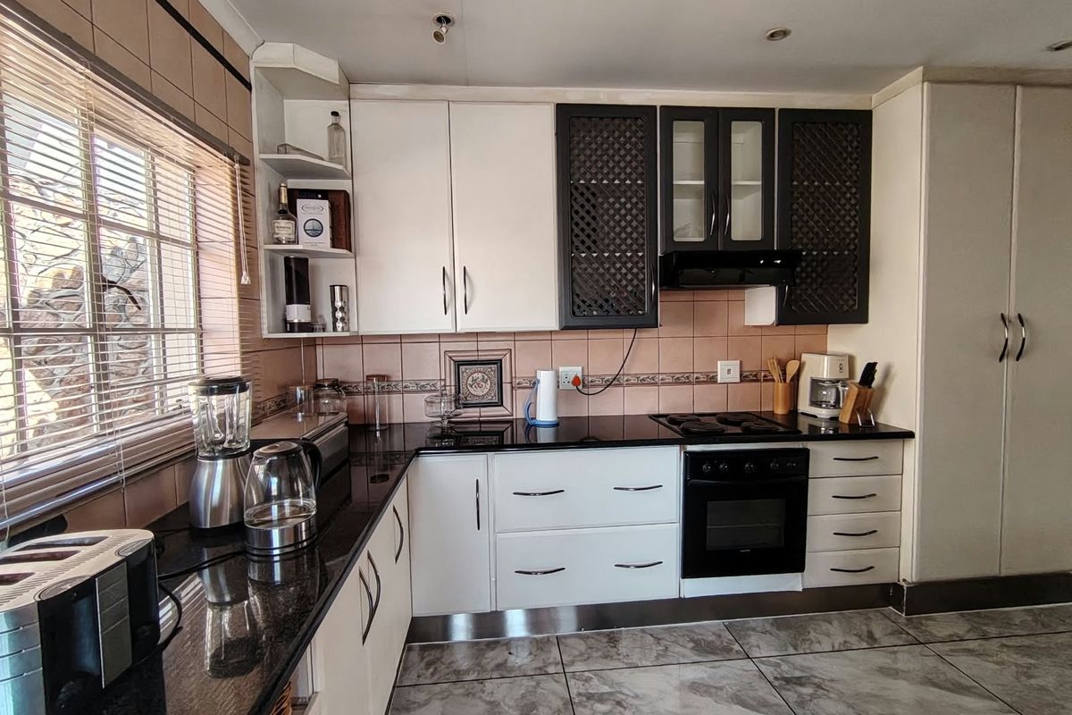 A functional kitchen featuring granite countertops, built-in oven, hob, extractor fan, and tiled flooring with ample storage cabinetry.