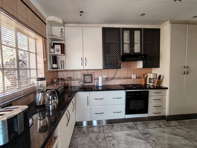 A functional kitchen featuring granite countertops, built-in oven, hob, extractor fan, and tiled flooring with ample storage cabinetry.