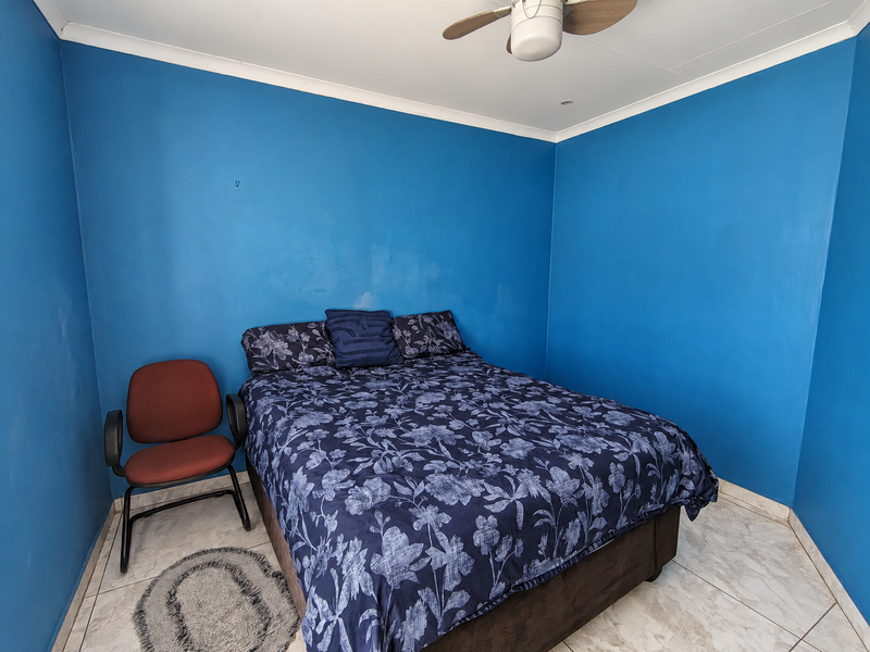 A bedroom featuring tiled flooring, a ceiling fan, and bold blue painted walls, offering a functional space ready for a modern aesthetic update.