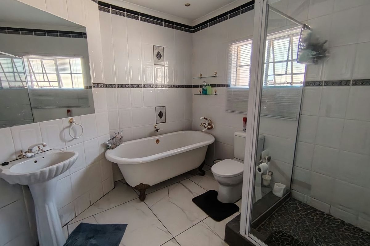 A well-appointed bathroom featuring a classic clawfoot bathtub, a separate shower enclosure, a pedestal basin, and neutral wall tiling with decorative accents.