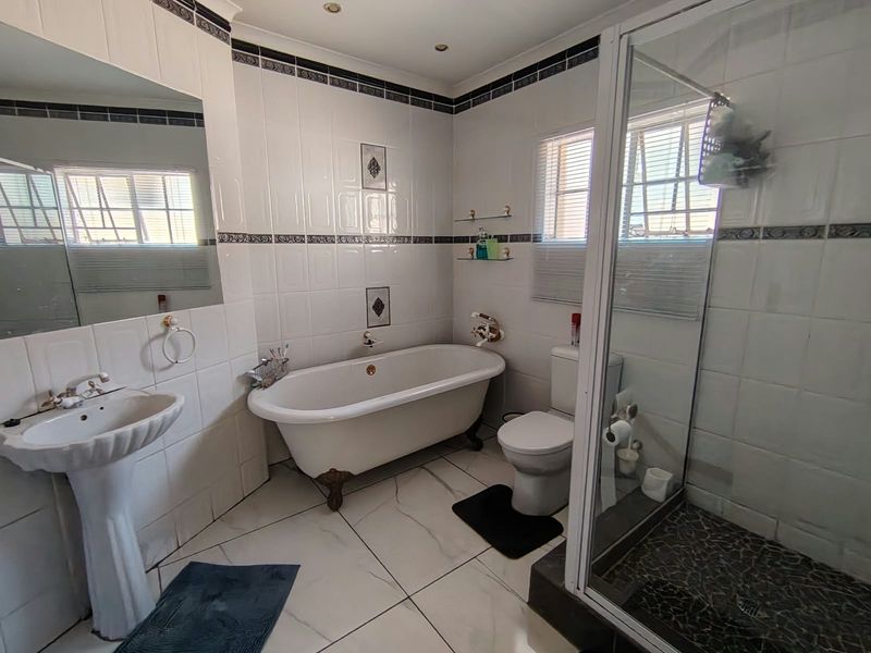 A well-appointed bathroom featuring a classic clawfoot bathtub, a separate shower enclosure, a pedestal basin, and neutral wall tiling with decorative accents.