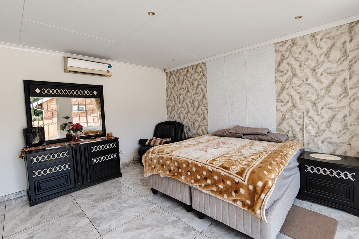 A well-maintained bedroom featuring tiled flooring, a decorative wallpaper accent wall, and a wall-mounted air conditioning unit.
