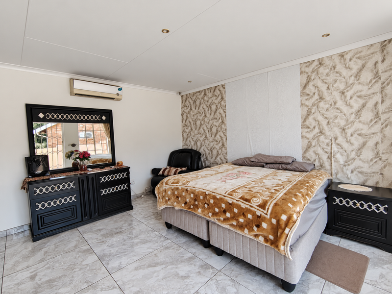A well-maintained bedroom featuring tiled flooring, a decorative wallpaper accent wall, and a wall-mounted air conditioning unit.