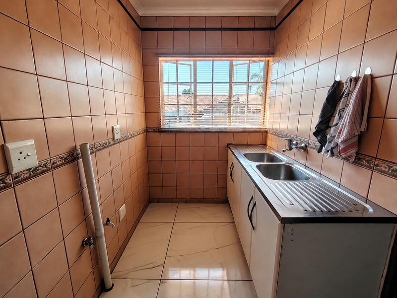 A functional laundry room featuring a double stainless steel sink, tiled walls, and tiled flooring with dedicated plumbing connections.