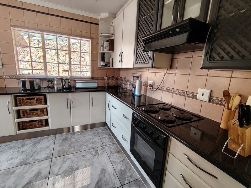 A functional kitchen featuring white cabinetry, dark granite countertops, a built-in oven with hob, and tiled finishes throughout.