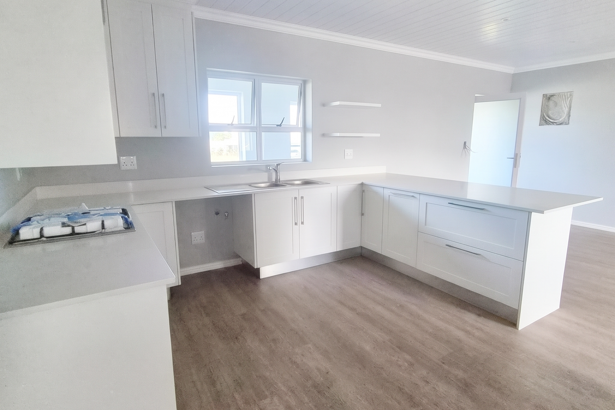 A bright, modern kitchen featuring white cabinetry, stone countertops, and wood-look laminate flooring, offering a clean and functional space ready for personalization.