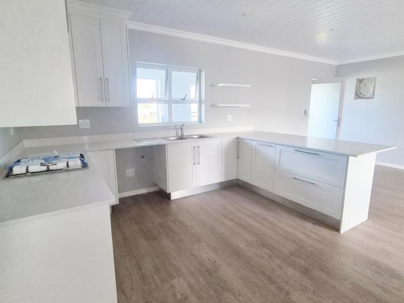 A bright, modern kitchen featuring white cabinetry, stone countertops, and wood-look laminate flooring, offering a clean and functional space ready for personalization.