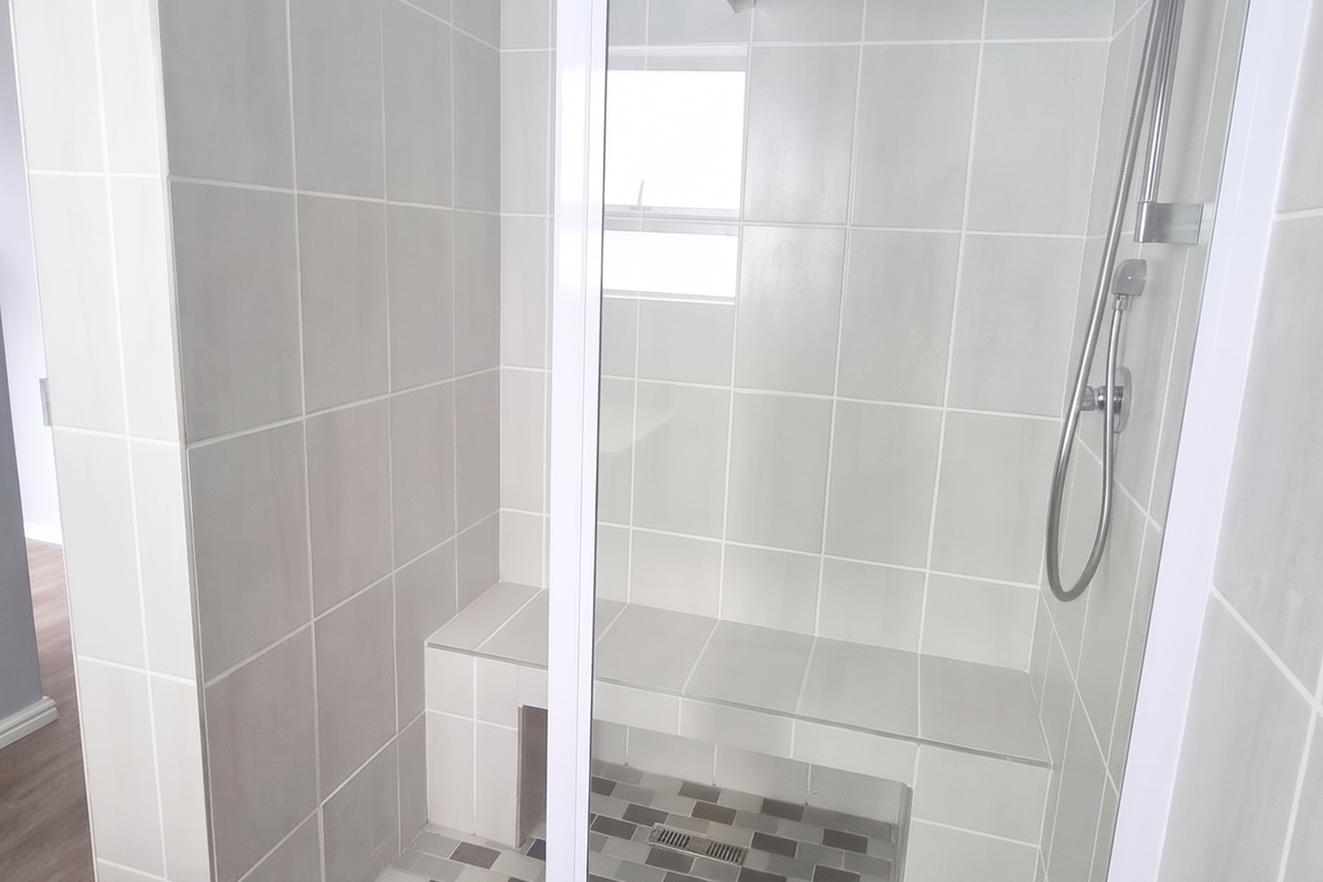 A modern, clean bathroom featuring a spacious walk-in shower with a built-in tiled bench, glass enclosure, and contemporary mosaic floor tiling.