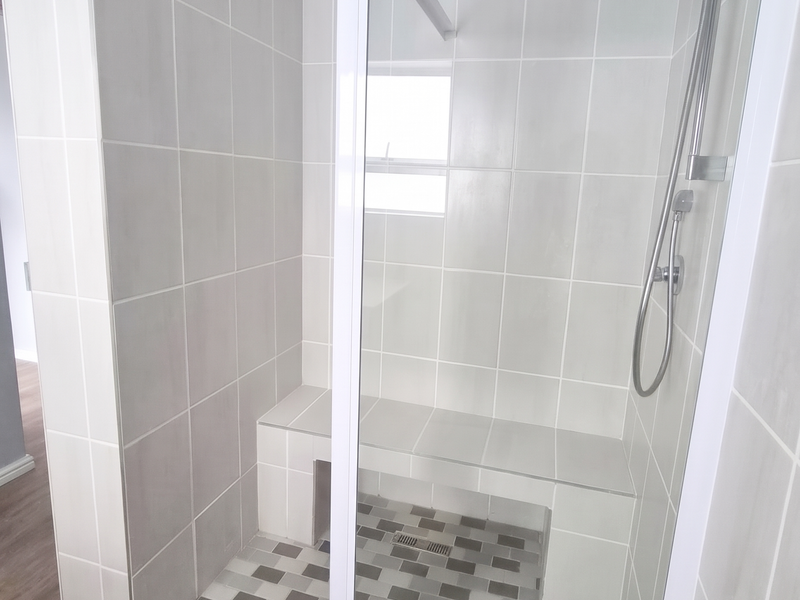 A modern, clean bathroom featuring a spacious walk-in shower with a built-in tiled bench, glass enclosure, and contemporary mosaic floor tiling.