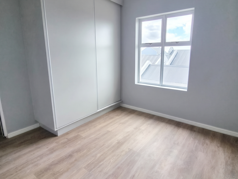 A bright, empty bedroom featuring modern laminate flooring, a built-in sliding wardrobe, and a tongue and groove ceiling with cornice detailing.