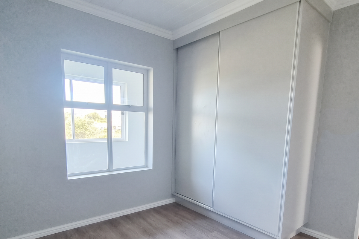 A bright, empty bedroom featuring modern laminate flooring, a built-in wardrobe, and a classic timber ceiling with decorative cornice.