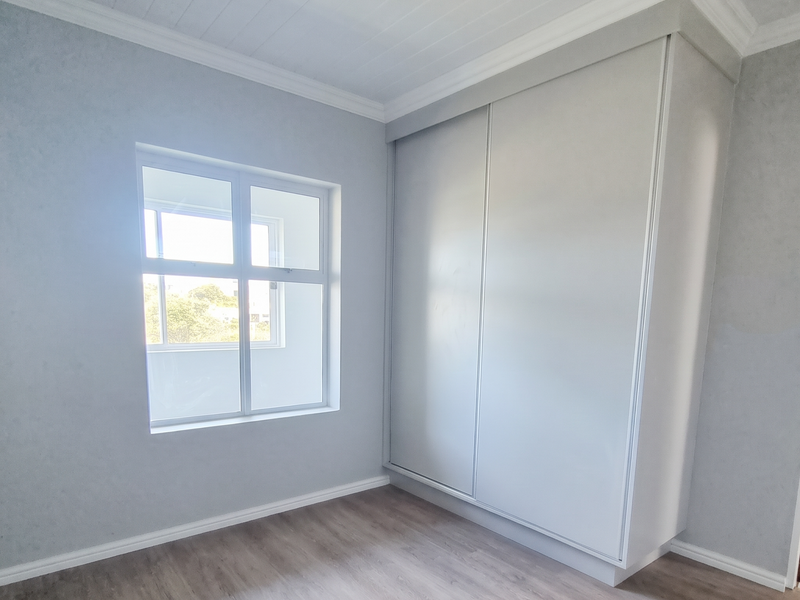 A bright, empty bedroom featuring modern laminate flooring, a built-in wardrobe, and a classic timber ceiling with decorative cornice.