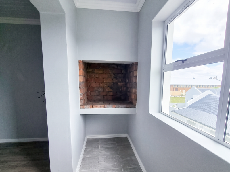 A bright, empty balcony or patio area featuring a built-in brick fireplace, tiled hearth, and modern laminate flooring with views of the surrounding neighborhood.