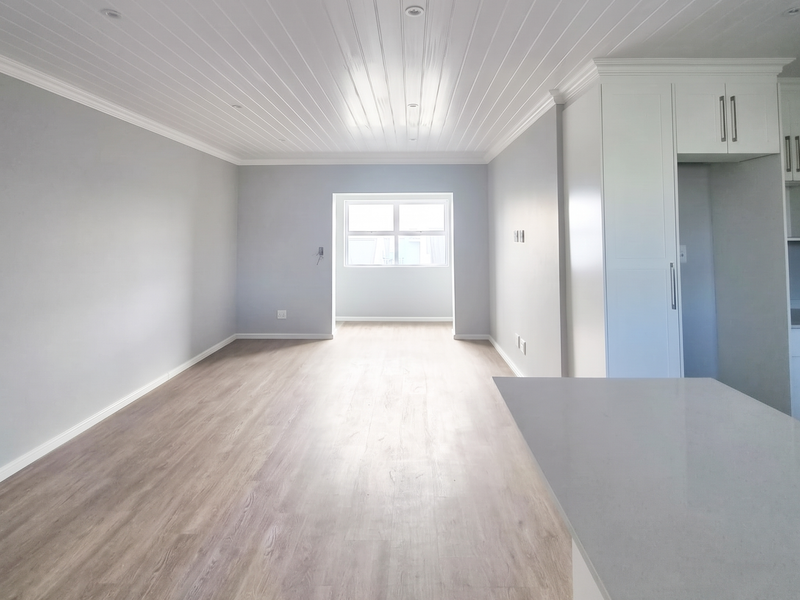 Spacious open-plan living area featuring modern laminate flooring, a white tongue and groove ceiling, and a sleek kitchen section with stone countertops.