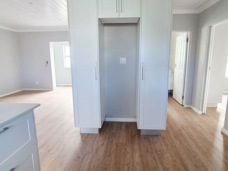Bright open-plan living area featuring modern white built-in cabinetry, light wood-look laminate flooring, and a clean tongue and groove ceiling finish.