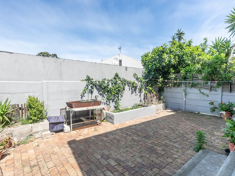 A private rear courtyard featuring brick paving, a raised garden bed, and high boundary walls, offering a functional outdoor space for the apartment.
