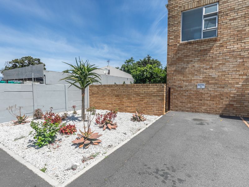 Exterior view of the apartment building featuring a face brick facade, paved driveway, and a landscaped garden area with boundary walls.