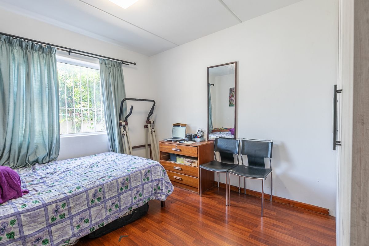 A bedroom featuring laminate flooring, a built-in cupboard, and a window fitted with security bars.