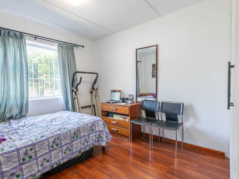 A bedroom featuring laminate flooring, a built-in cupboard, and a window fitted with security bars.