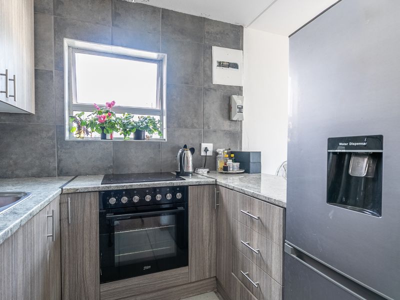 Modern kitchen featuring wood-grain cabinetry, granite countertops, a tiled backsplash, and integrated electric oven and hob.
