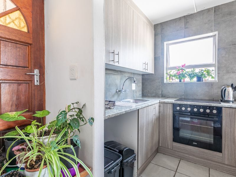 Compact kitchen featuring modern wood-look cabinetry, built-in oven and hob, tiled backsplash, and direct access to the main entrance.