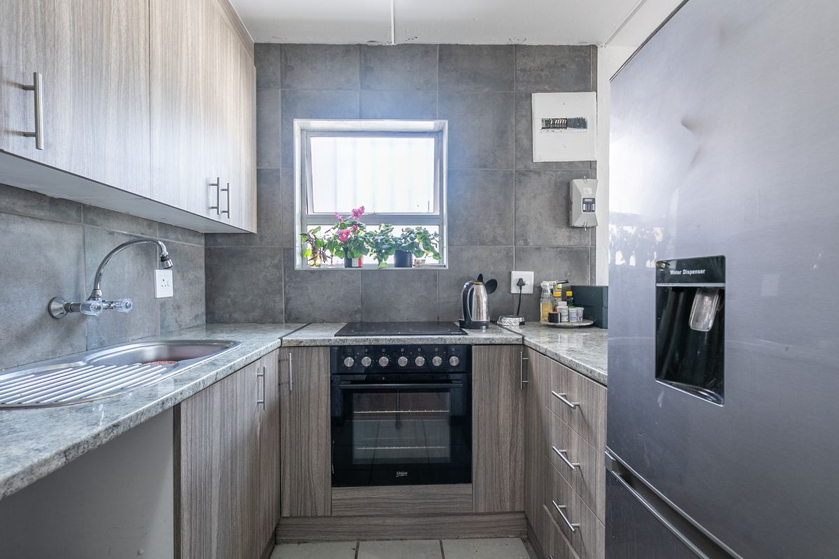 A functional kitchen featuring wood-look cabinetry, granite countertops, a tiled backsplash, and integrated electric oven and hob.