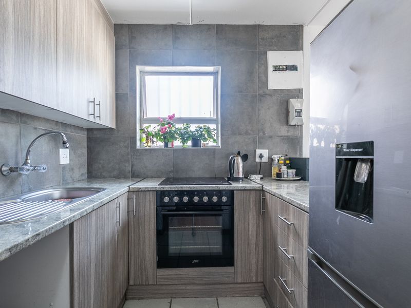 A functional kitchen featuring wood-look cabinetry, granite countertops, a tiled backsplash, and integrated electric oven and hob.