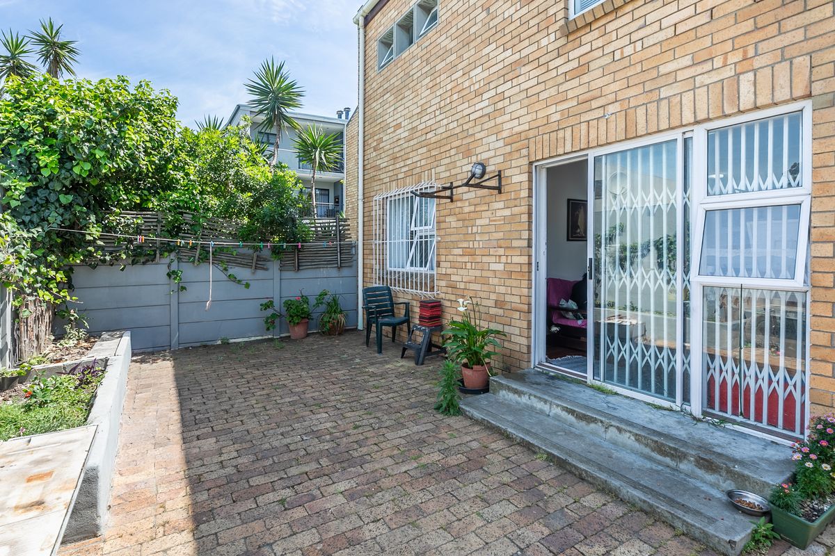 A rear courtyard featuring brick paving, a raised garden bed, and a sliding door entrance with security gate access to the apartment interior.