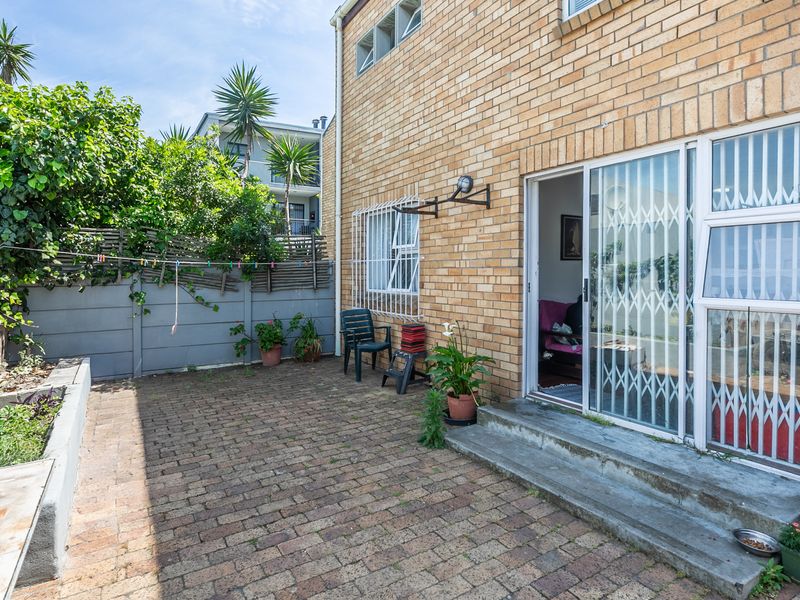 A rear courtyard featuring brick paving, a raised garden bed, and a sliding door entrance with security gate access to the apartment interior.