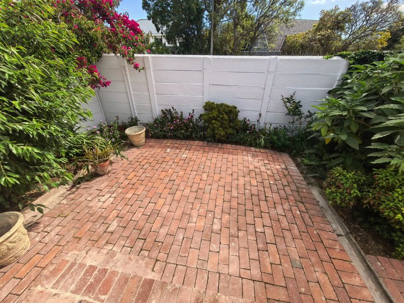 A private outdoor patio area featuring red brick paving, enclosed by a secure precast concrete boundary wall with established garden borders.