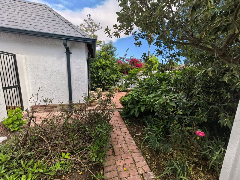 A rear garden area featuring a brick paved pathway leading to a patio, adjacent to the townhouse exterior with a slate roof.