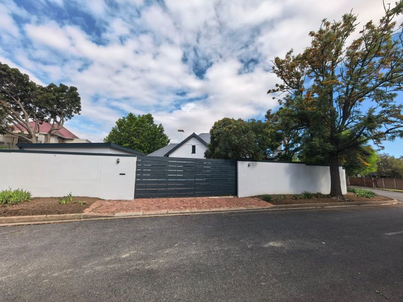 Front view of the property featuring a secure perimeter wall, a modern horizontal slat driveway gate, and a brick-paved entrance area.