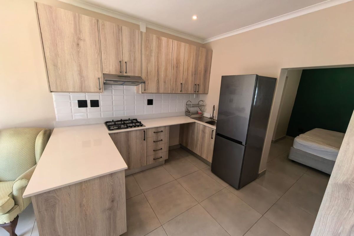 Modern kitchen featuring light wood-grain cabinetry, quartz countertops, gas hob, extractor fan, and subway tile backsplash, seamlessly integrated with tiled flooring.
