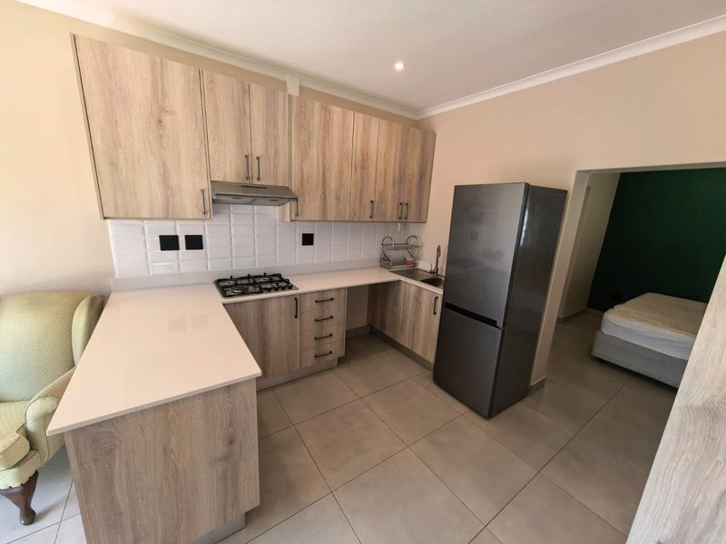 Modern kitchen featuring light wood-grain cabinetry, quartz countertops, gas hob, extractor fan, and subway tile backsplash, seamlessly integrated with tiled flooring.
