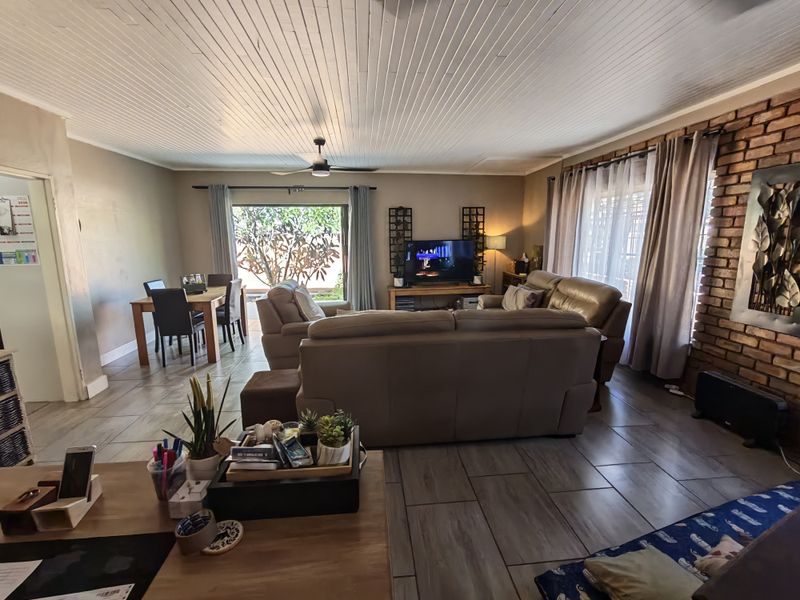 Spacious open-plan living and dining area featuring tiled floors, a timber ceiling, and an exposed brick feature wall with access to the garden.