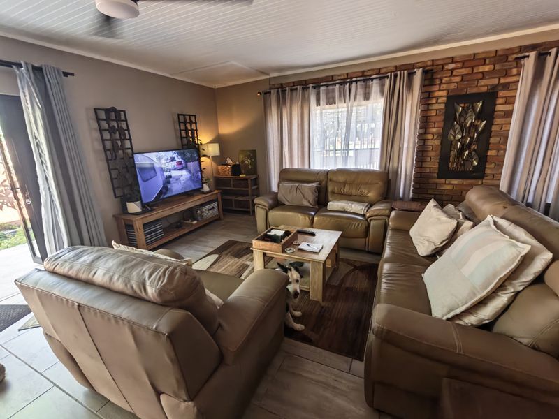A comfortable living room featuring an exposed brick accent wall, tiled flooring, and a tongue and groove ceiling with access to an outdoor area.